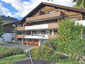 A multi-story building with a balcony, a swing set, and a well-maintained garden. - Baldrian C14 Appartement/Fewo, Bad, WC, 3 Schlafräume 4.5- Zimmerwohnung by Interhome (Adelboden)