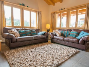 A living room with two brown leather sofas, a patterned rug, and large windows with curtains. - Schützenrain DG Appartement/Fewo, Dusche und Bad, WC, 4 oder mehr Schlafräume by Interhome (Adelboden)