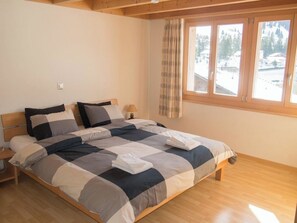 A bedroom with a large bed, wooden headboard, a nightstand, a lamp, and a window with curtains. - Schützenrain DG Appartement/Fewo, Dusche und Bad, WC, 4 oder mehr Schlafräume by Interhome (Adelboden)