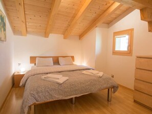 A bedroom with a wooden ceiling, a bed with a checkered bedspread, a nightstand, and a dresser. - Schützenrain DG Appartement/Fewo, Dusche und Bad, WC, 4 oder mehr Schlafräume by Interhome (Adelboden)