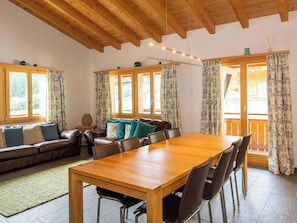 A spacious room with a wooden dining table, leather sofas, and large windows with curtains. - Schützenrain DG Appartement/Fewo, Dusche und Bad, WC, 4 oder mehr Schlafräume by Interhome (Adelboden)