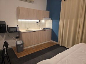 A compact kitchenette with a microwave, sink, and a small trash bin.