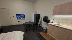 Ett kompakt hotellrum med en säng, ett litet matbord, en TV som är monterad på väggen, en mikrovågsugn och ett handfat.