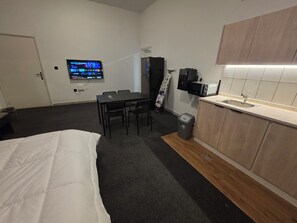 Habitación de hotel compacta con cama, una pequeña mesa de comedor, televisor montado en la pared, microondas y lavamanos.