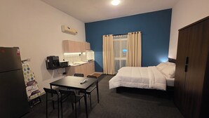 Ett kompakt hotellrum med ett litet kök, en säng, ett matbord med stolar och en garderob.