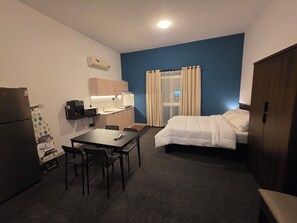 A compact hotel room with a kitchenette, a bed, a dining table with chairs, and a wardrobe.
