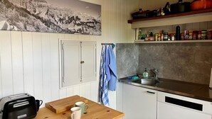 Ett kök med vita skåp, ett träbord, en brödrost, ett handfat och en hylla med kastruller.