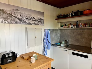 Eine Küche mit weißen Schränken, einem Holztisch, einem Toaster, einer Spüle und einem Regal mit Kochtöpfen.