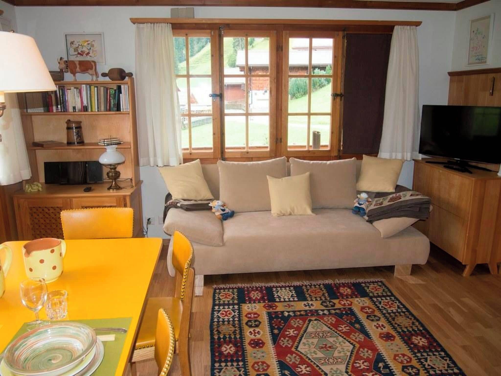 Ein gemütliches Wohnzimmer mit Sofa, Fernseher, Bücherregal und einem Essbereich mit Tisch und Stühlen.