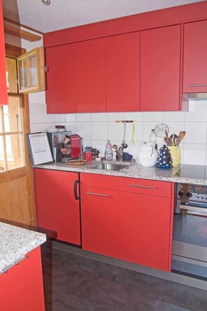 A kitchen with red cabinets, a granite countertop, and a stainless steel oven. - Chalet Zwirbeli Appartement/Fewo, Dusche, WC, 1 Schlafraum 2-Zimmerwohnung by Interhome (Adelboden)