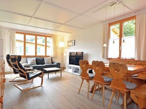 Ein modernes Wohnzimmer mit einer Couch, einem Fernseher, Holzstühlen und einem Esstisch.