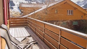 Eine Holzdielen-Terrasse mit Blick auf schneebedeckte Berge und eine Chalet-Hütte.