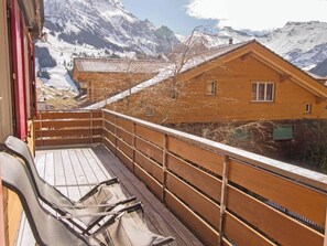 Eine Holzdielen-Terrasse mit Blick auf schneebedeckte Berge und eine Chalet-Hütte.