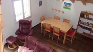 Ett rum med ett matbord i trä, fyra stolar, en soffa i läder, en bokhylla och ett fönster.