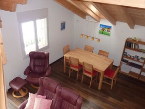 Ein Zimmer mit einem Holztisch, vier Stühlen, einem Ledersofa, einem Bücherregal und einem Fenster.