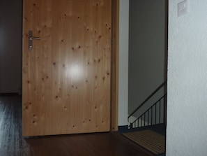 A wooden door with a metal handle, a staircase with a black railing, and a white textured wall. - Chalet Kanderblick Appartement/Fewo, Bad, WC, Balkon by Interhome (Kandersteg)