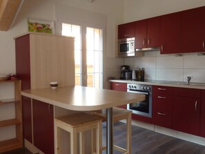A kitchen with a wooden bar counter, red cabinets, a stainless steel oven, and a microwave. - Chalet Kanderblick Appartement/Fewo, Bad, WC, Balkon by Interhome (Kandersteg)