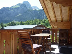 A wooden deck with a table and chairs, overlooking a mountain.