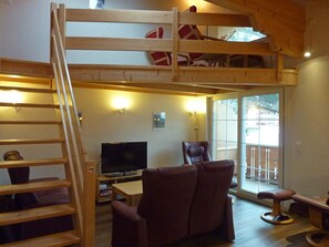 A loft-style room with a wooden ladder, a television, a brown leather chair, and a sliding glass door leading to an outdoor area.