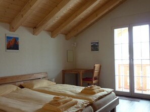 A room with a wooden ceiling, two beds with neatly folded towels, a wooden chair, and a window with a view.