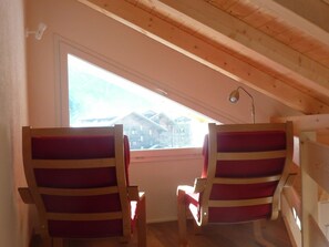 A room with two wooden chairs with red cushions, a small table, and a window with a view of buildings.