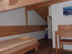 A small, cozy room with a wooden bench, a single bed, and a chair.