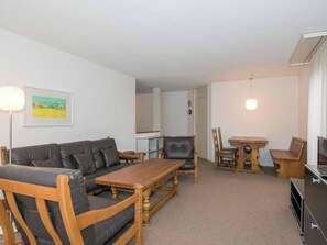 Ein Wohnzimmer mit einer Couch, einem Holztisch, einem schwarzen Ledersessel, einem Esstisch mit Stühlen und einem Gemälde an der Wand.