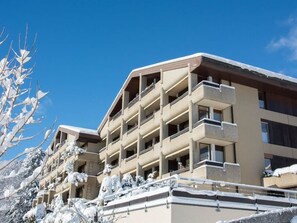 Ein mehrstöckiges Hotel mit Balkonen, schneebedeckten Bäumen und blauem Himmel.