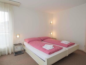 Ein Zimmer mit einem Einzelbett, einer karierten Bettdecke, Nachttischlampen, einem kleinen Nachttisch und einem Fenster mit Vorhängen.