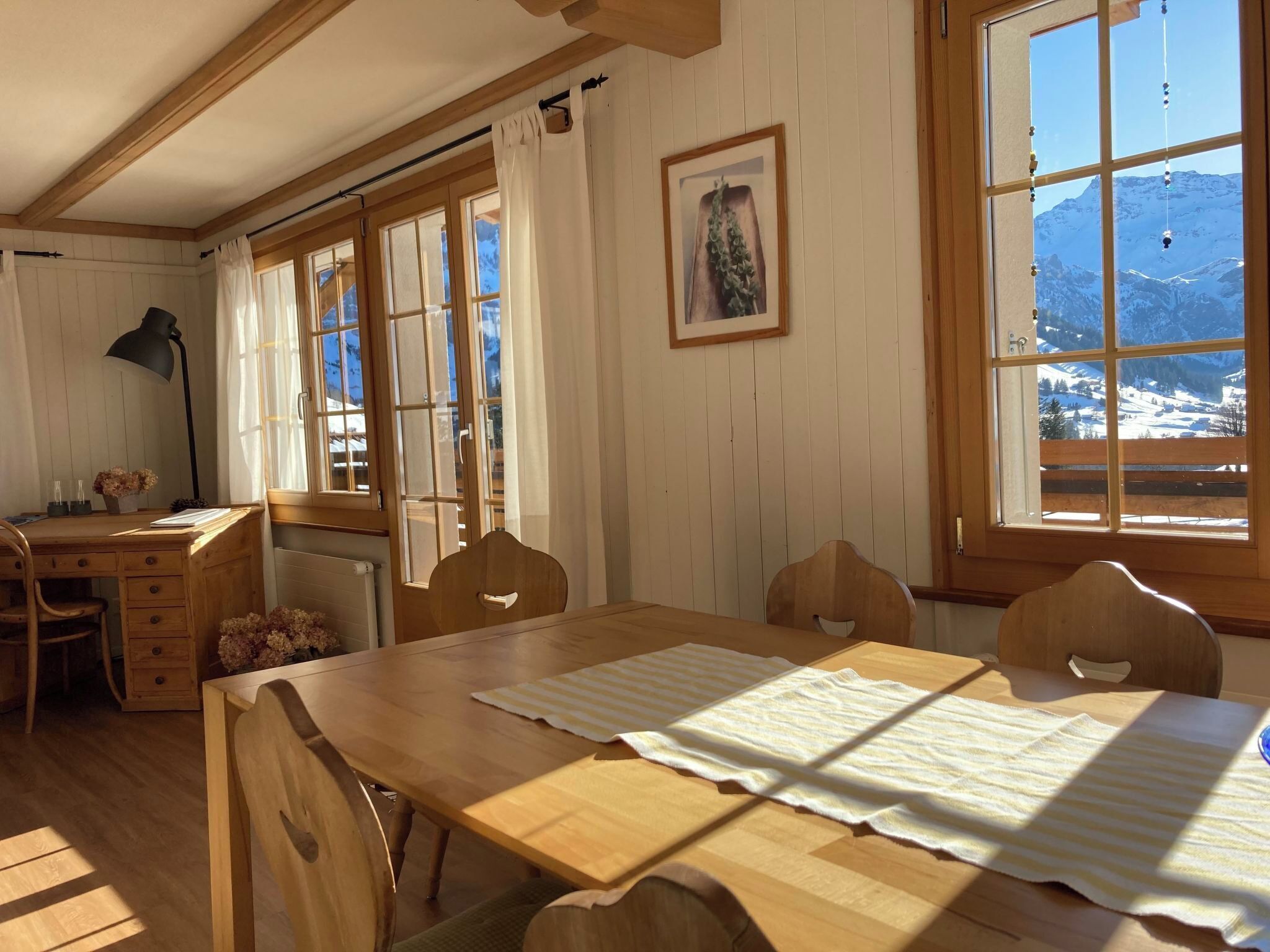 Une pièce avec une table en bois, des chaises, un bureau et une fenêtre donnant sur la montagne.