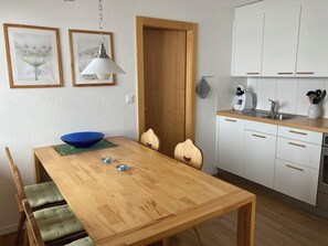 Une cuisine de taille réduite avec des meubles blancs, une table à manger en bois et un saladier bleu.
