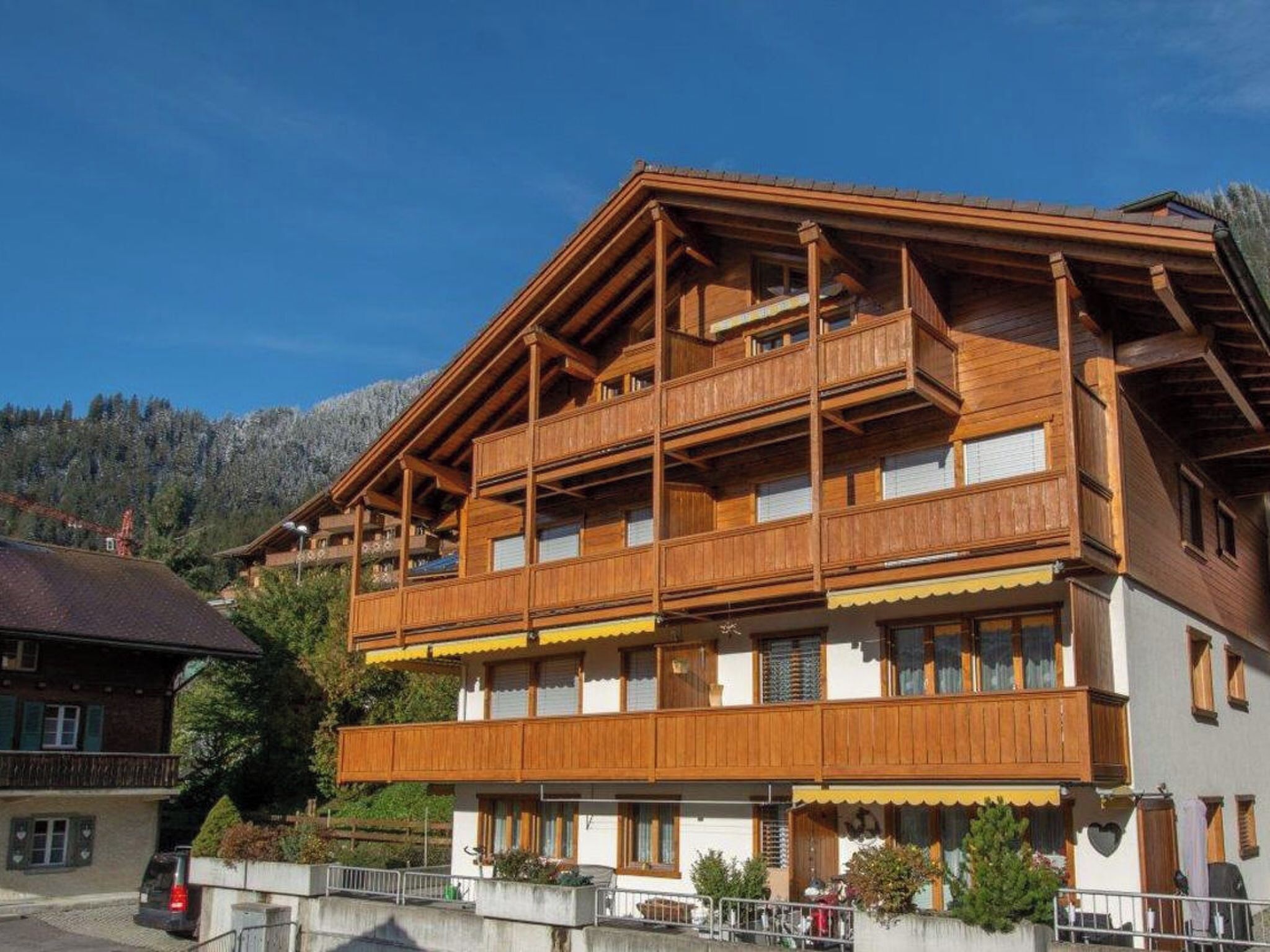 A multi-story wooden building with balconies, a sloped roof, and a mountainous backdrop.