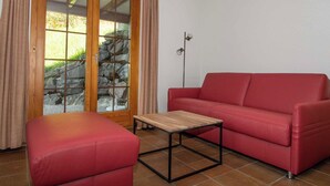Ein Zimmer mit einer roten Couch, einem Holztisch, einer Steinsäule und einem Fenster mit Vorhängen.