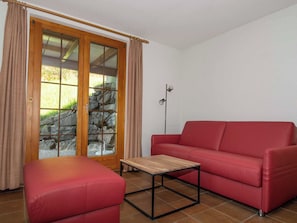 Ein Zimmer mit einer roten Couch, einem Holztisch, einer Steinsäule und einem Fenster mit Vorhängen.