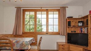 Ein Zimmer mit einem Esstisch, Stühlen, einem Fernseher und einem Bücherregal.