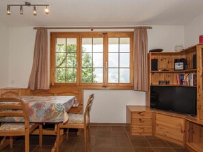 Ein Zimmer mit einem Esstisch, Stühlen, einem Fernseher und einem Bücherregal.