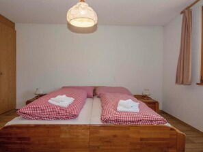 A room with a wooden bed, two bedside tables, a hanging light fixture, and a window with curtains. - Senggi Appartement/Fewo, Dusche, WC, 1 Schlafraum 2-Zimmerwohnung by Interhome (Adelboden)