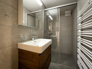 Ein modernes Badezimmer mit einem weißen Waschbecken, einem Spiegel und einer Duschkabine aus Glas.