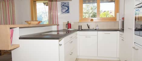 Cocina compacta con armarios blancos, encimera negra, ventana con vistas y extractor de acero inoxidable.