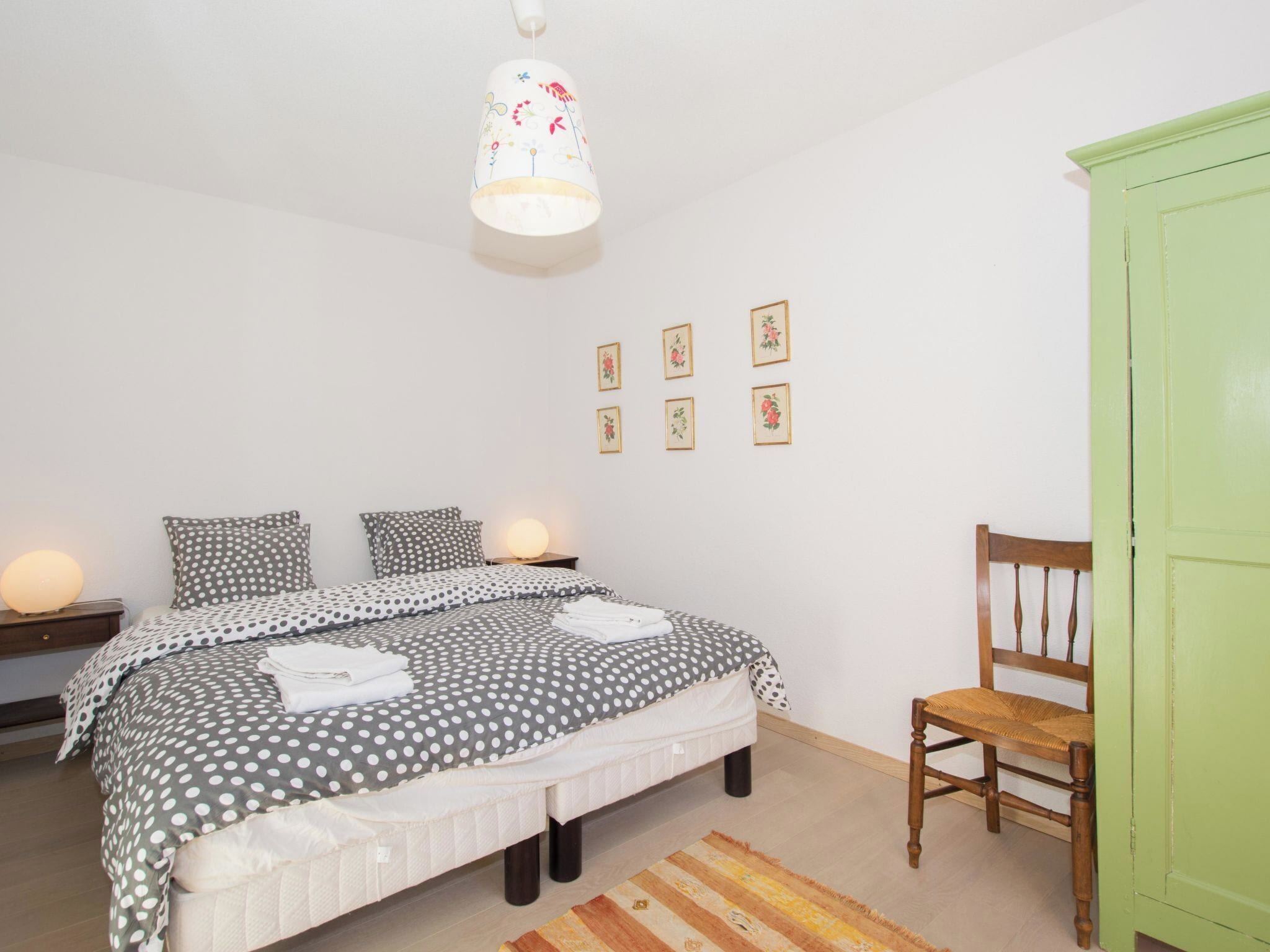 A bedroom with a bed, a chair, a wardrobe, and a wall with framed pictures.