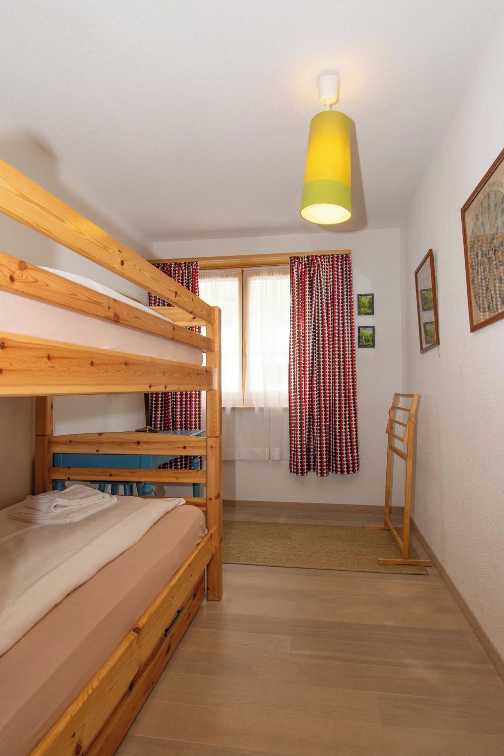 A room with bunk beds, a standing desk, a window with curtains, and a painting on the wall.
