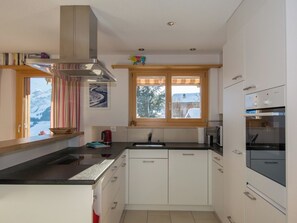 A modern kitchen with white cabinets, a black countertop, a stainless steel range hood, a window with a view of trees, and a built-in oven. - Gartenweg Appartement/Fewo, Dusche und Bad, WC, 4 oder mehr Schlafräume by Interhome (Adelboden)