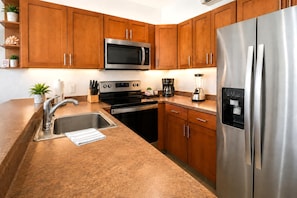 A modern kitchen with stainless steel appliances, wooden cabinets, and a granite countertop. - Napili Point | 1-Bedroom Oceanfront Villa | Car Incl. w/ 6+ Nights | NAP-B31 by KBM (Lahaina)