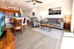 A modern living room with a grey sofa, a wooden coffee table, and a dining area with wooden chairs and a table. - Napili Point | 1-Bedroom Oceanfront Villa | Car Incl. w/ 6+ Nights | NAP-B31 by KBM (Lahaina)