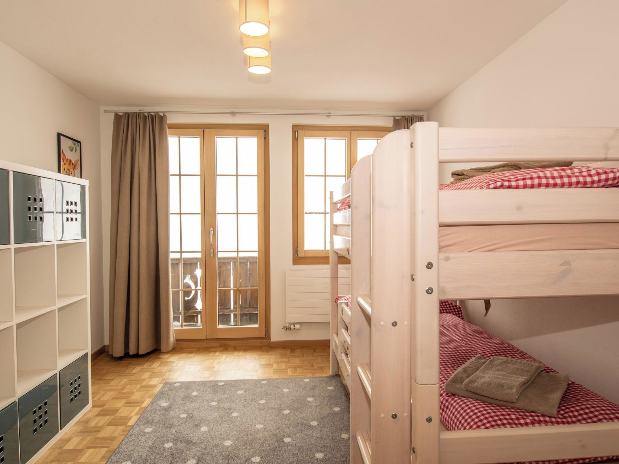 Une chambre avec un lit superposé, une armoire avec plusieurs compartiments, un radiateur et une fenêtre avec des rideaux.