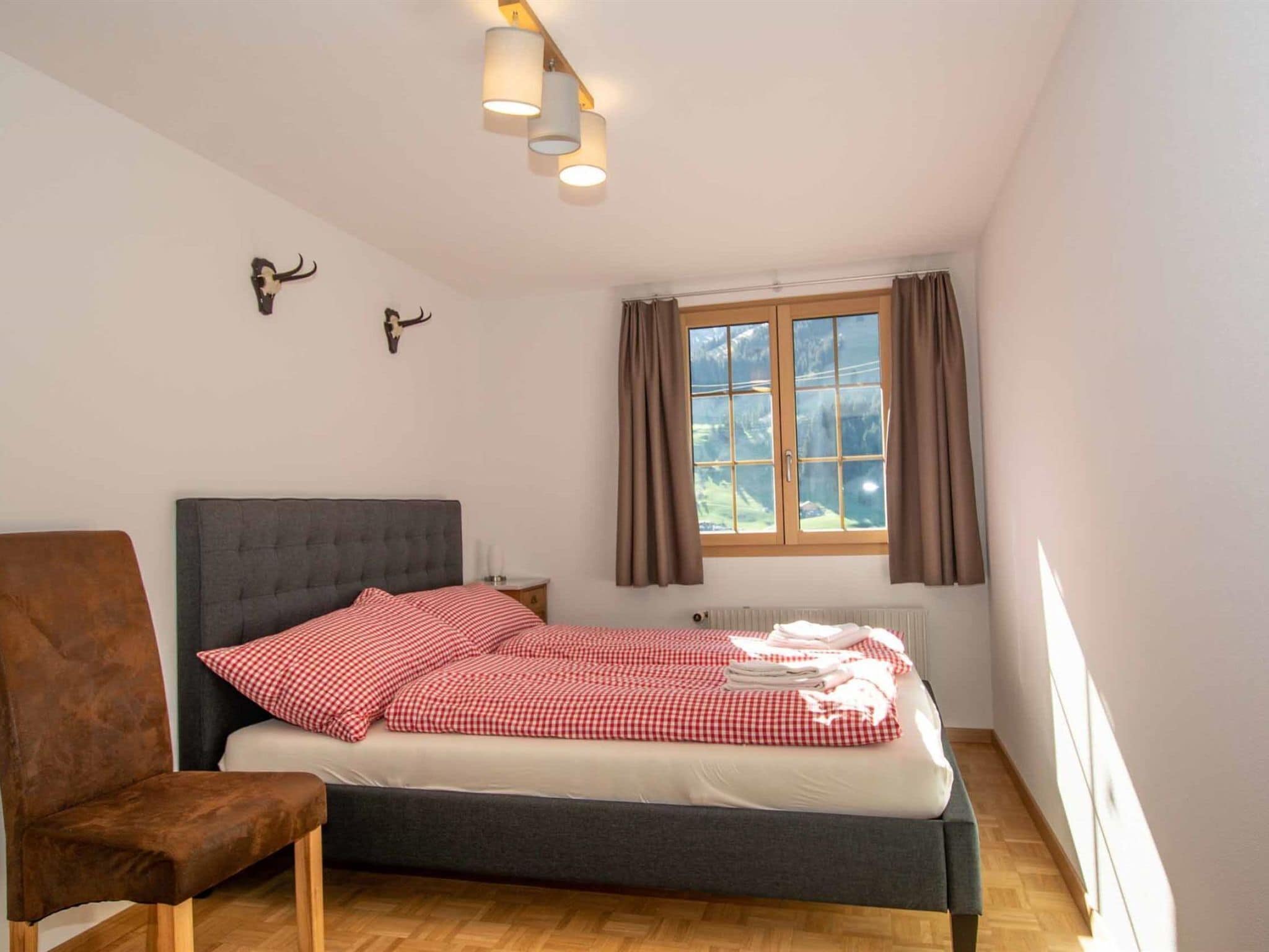 A bedroom with a bed, a chair, a window with curtains, and wall-mounted lights.