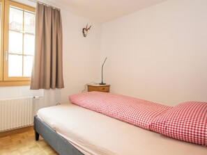 A single-bed room with a checkered bedspread, a window with curtains, a radiator, and a wall-mounted deer skull decoration. - Am Strubelweg Appartement/Fewo, Dusche, WC, 3 Schlafräume 5.5-Zimmerwohnung by Interhome (Adelboden)