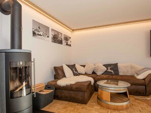 Ein gemütliches Wohnzimmer mit Kaminofen, einem braunen Ledersofa und einem runden Holztisch.