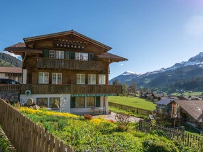 Eine zweistöckige Holzhütte mit Balkon, umgeben von einem Garten mit verschiedenen Pflanzen und Blumen.