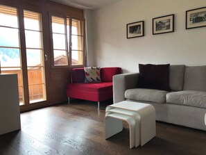 Un salon avec un canapé rouge, un canapé gris et un pouf blanc. Deux tableaux encadrés sont accrochés au mur.